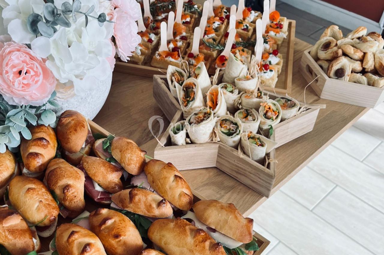 Plateau de mini-sandwichs, wraps et feuilletés disposés sur une table en bois, avec un bouquet de fleurs en arrière-plan.