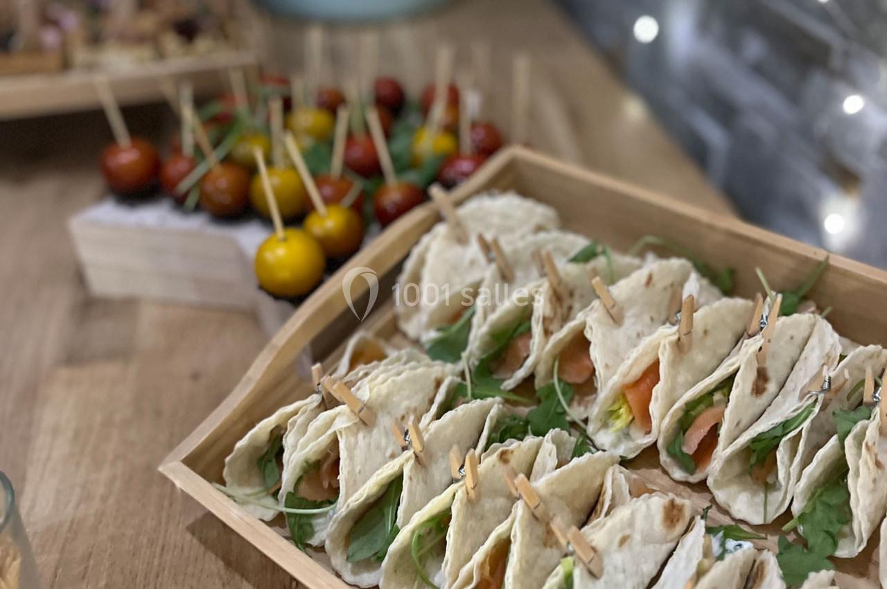 Plateau de mini-tacos garnis de saumon et roquette, avec en arrière-plan des brochettes de tomates cerises colorées.