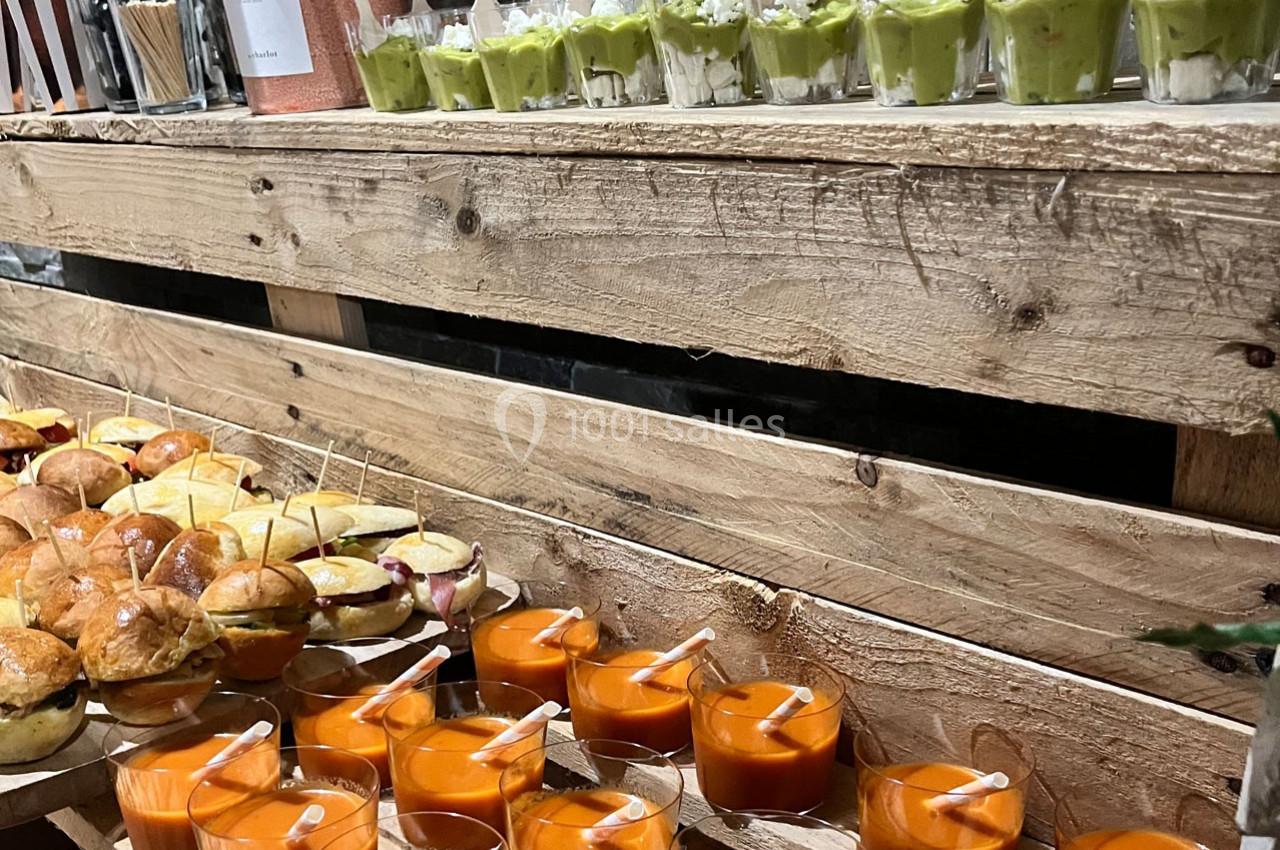 Plateau en bois avec verrines de soupe orange, guacamole et mini-sandwiches disposés pour un buffet.