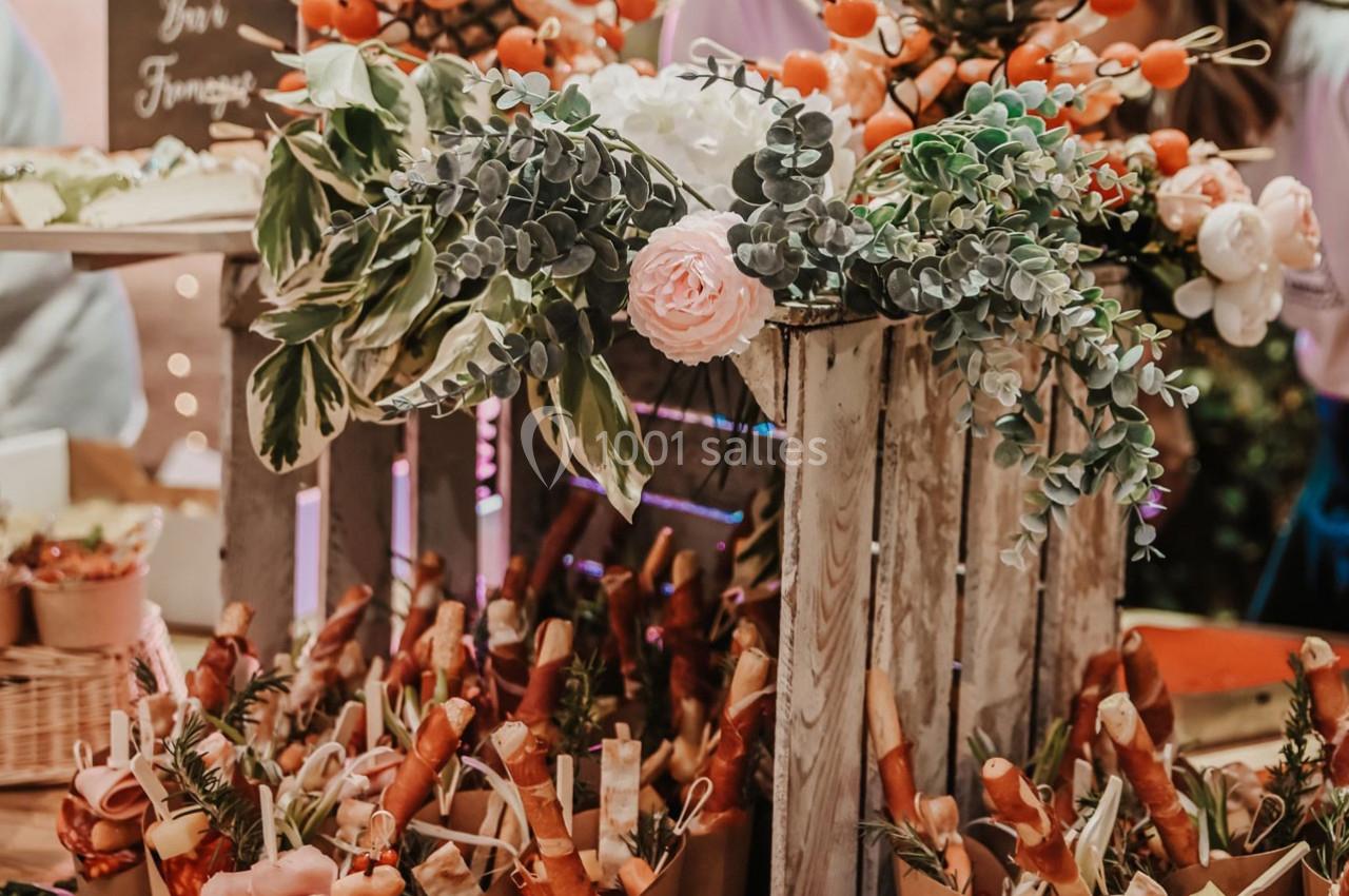 Présentoir décoré avec des fleurs et des plantes, entouré de cornets garnis de charcuterie et de fromage.
