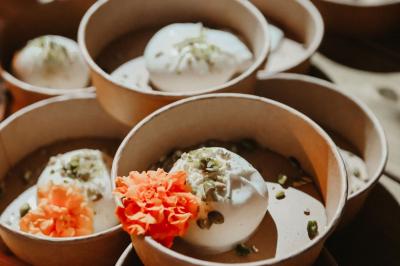 Des portions de nourriture servies dans des pots en carton avec des fleurs blanches en décoration.