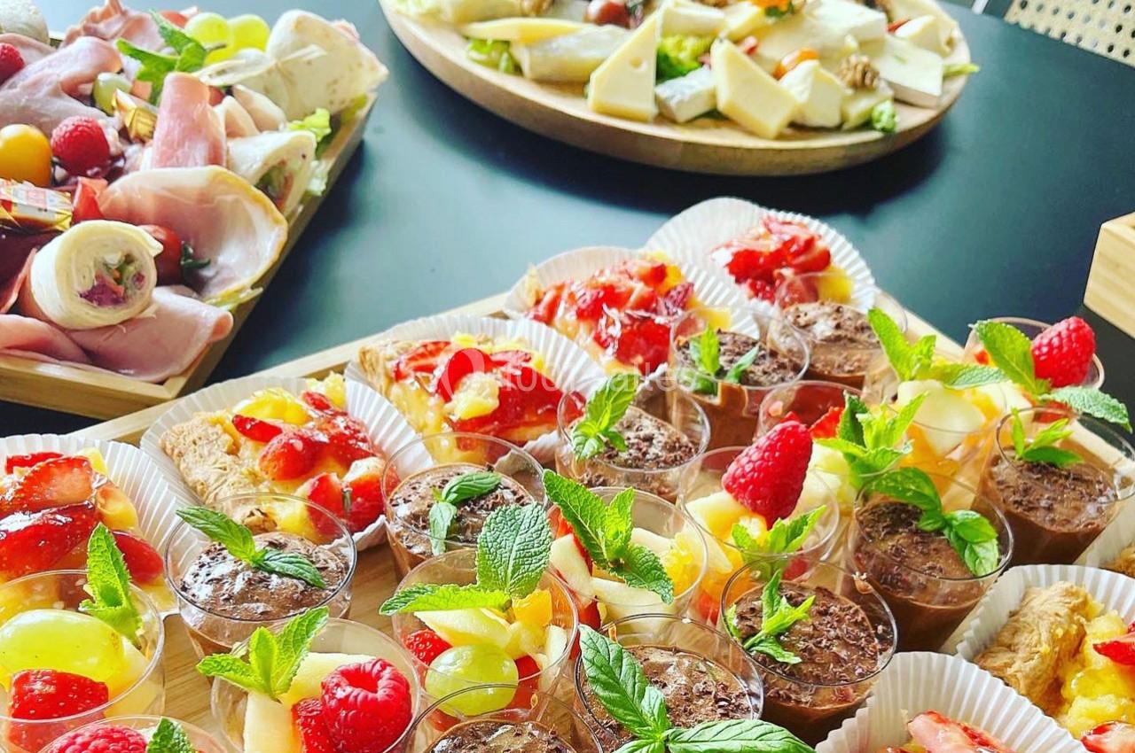 Plateaux de desserts variés avec fruits frais, crèmes et pâtisseries, accompagnés de charcuteries et fromages en arrière…