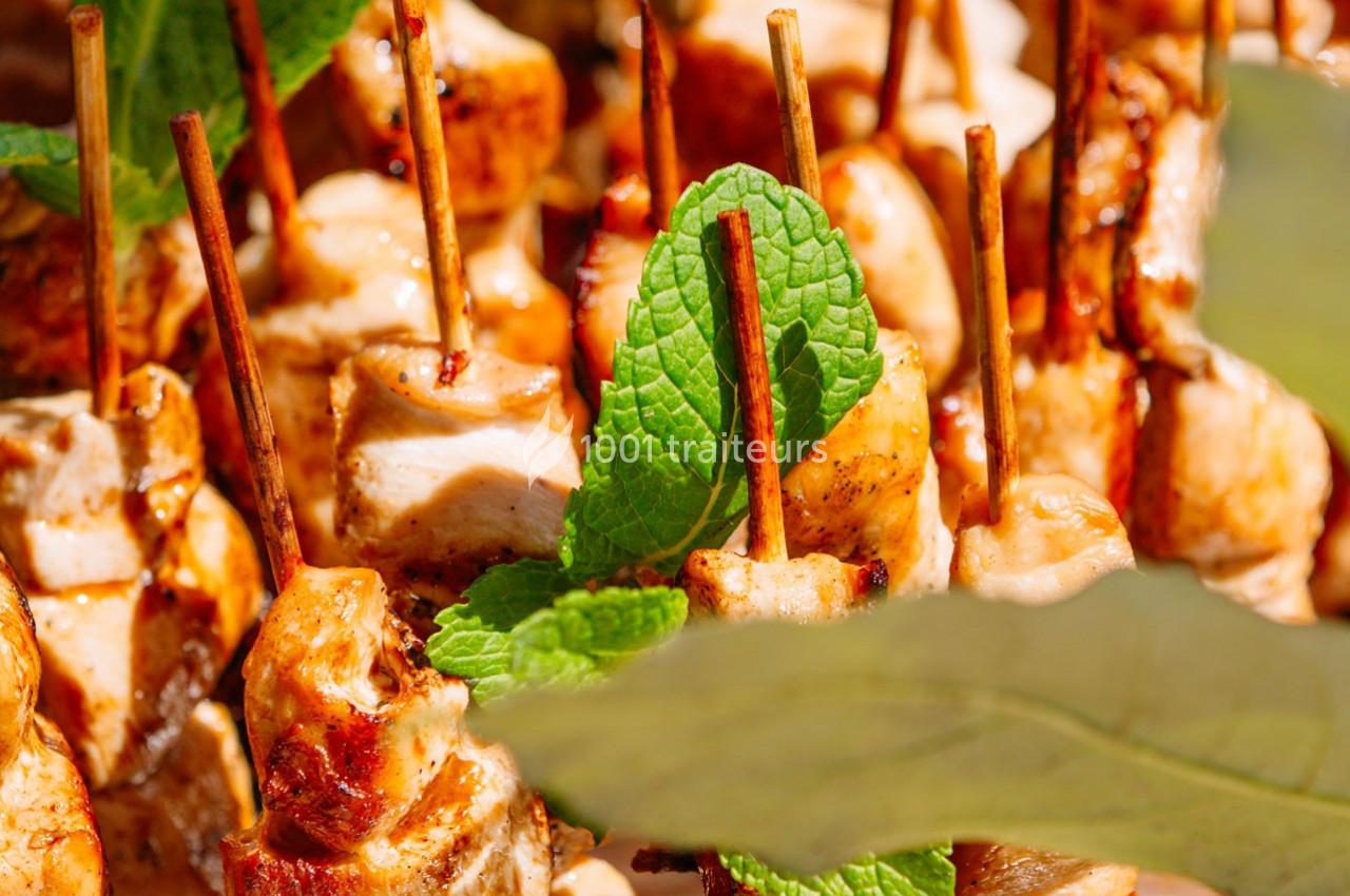 Brochettes de poulet grillé garnies de feuilles de menthe, présentées sur un plateau en plein air.
