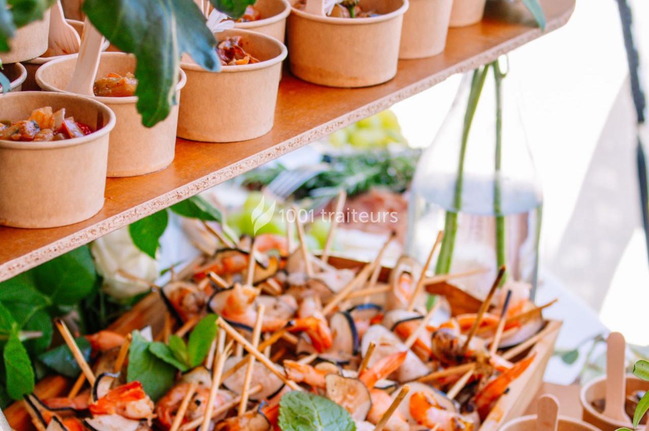 Plateau de brochettes et verrines disposés sur une table décorée de feuillage et de fleurs.