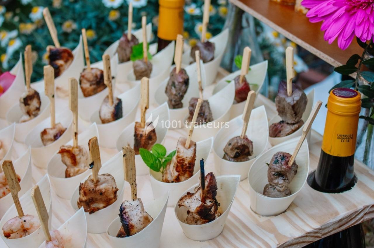 Brochettes de viande et fruits de mer présentées dans des coupelles individuelles sur une table en bois.