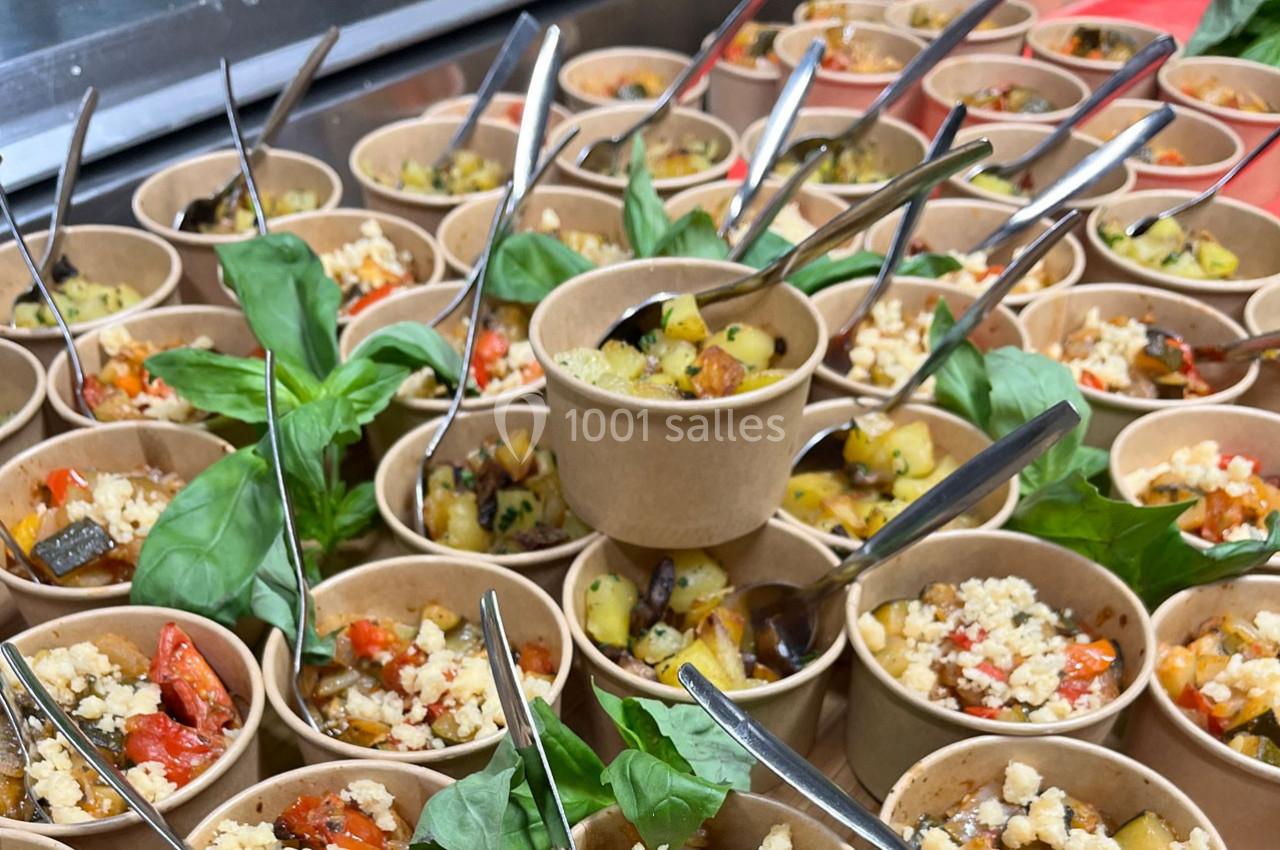 Petits bols en carton remplis de ratatouille garnie de crumble salé, décorés de feuilles de basilic frais.