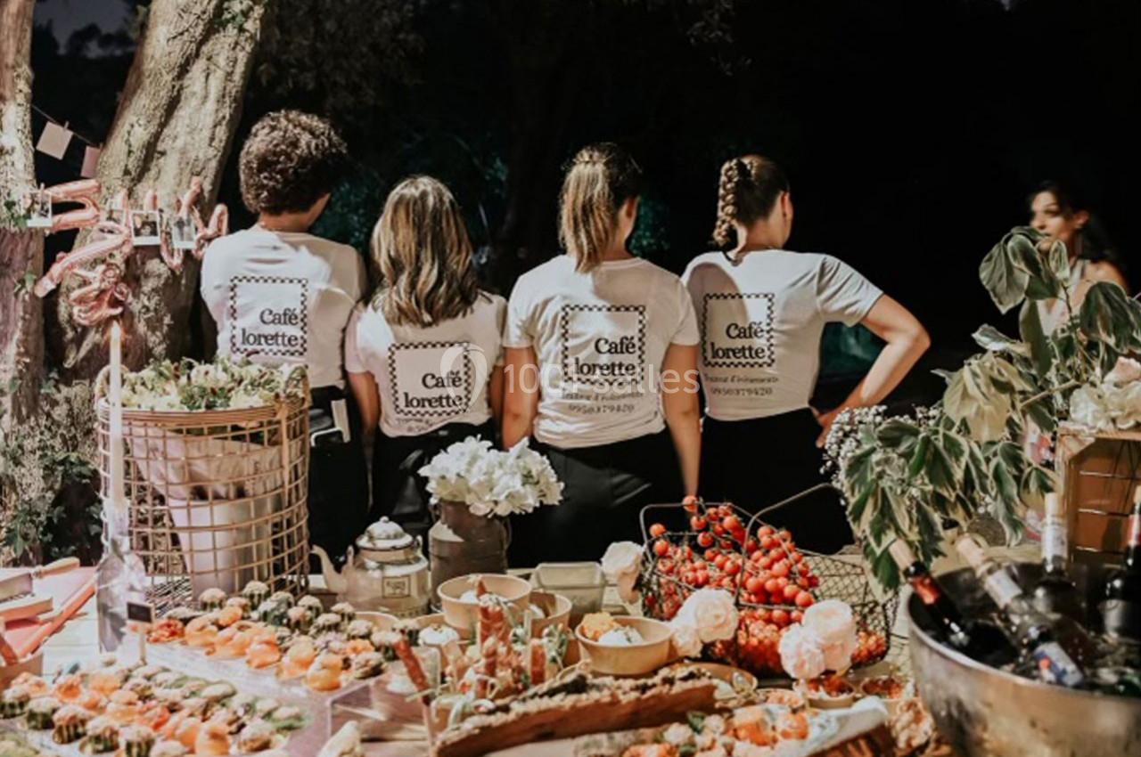 Quatre personnes de dos portant des t-shirts assortis, devant une table garnie de plats et boissons en extérieur.