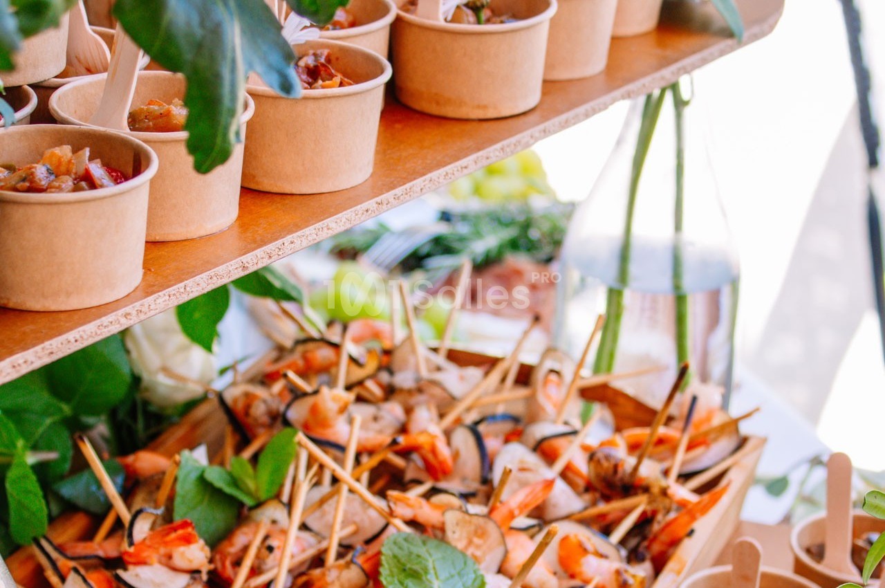 Plateau de brochettes et verrines disposés sur une table décorée de feuillage et de fleurs.