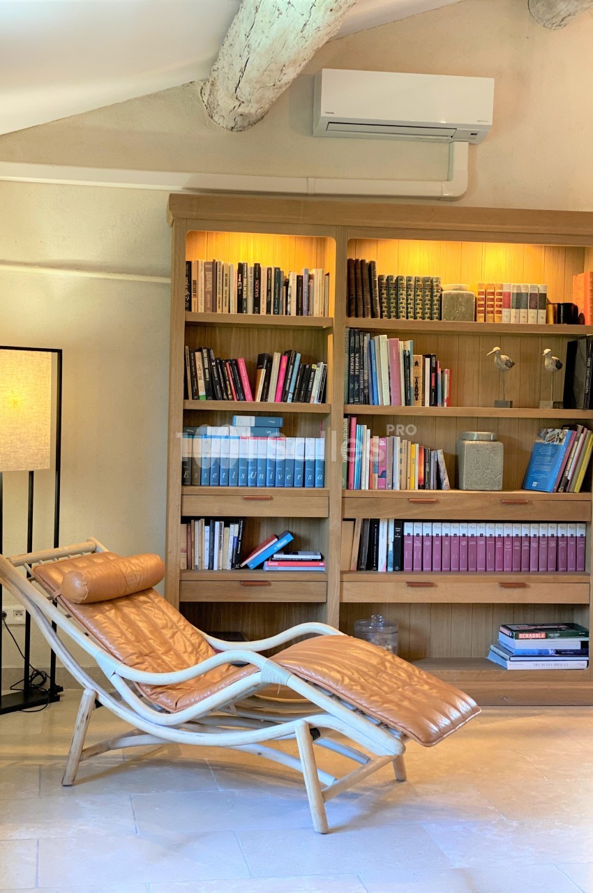 Bibliothèque en bois éclairée, remplie de livres, avec un fauteuil en cuir inclinable et une lampe dans un intérieur…