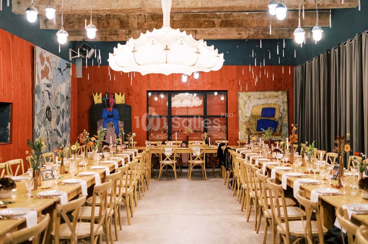 Salle de réception décorée avec des tables alignées, des chaises en bois, des fleurs et des œuvres d'art aux murs.