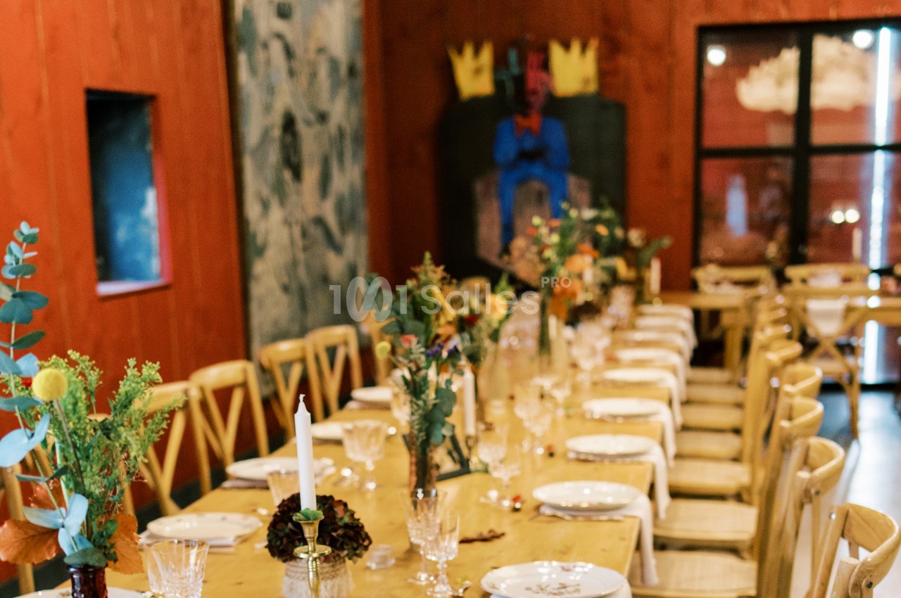 Salle de réception décorée avec des tables alignées, nappes blanches, bougies et arrangements floraux.