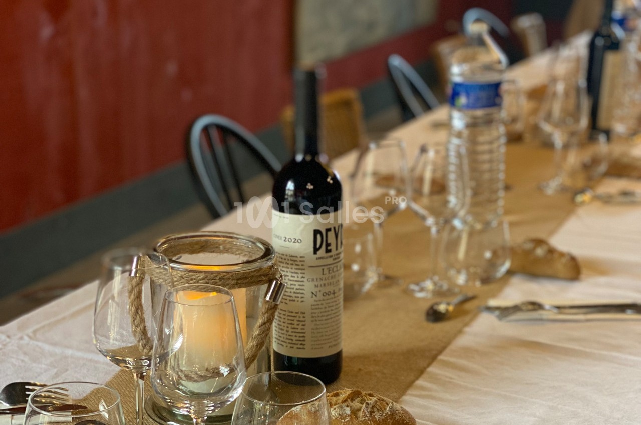 Bouteille de vin rouge, bougie allumée et verres disposés sur une table dressée avec nappe blanche et pain.