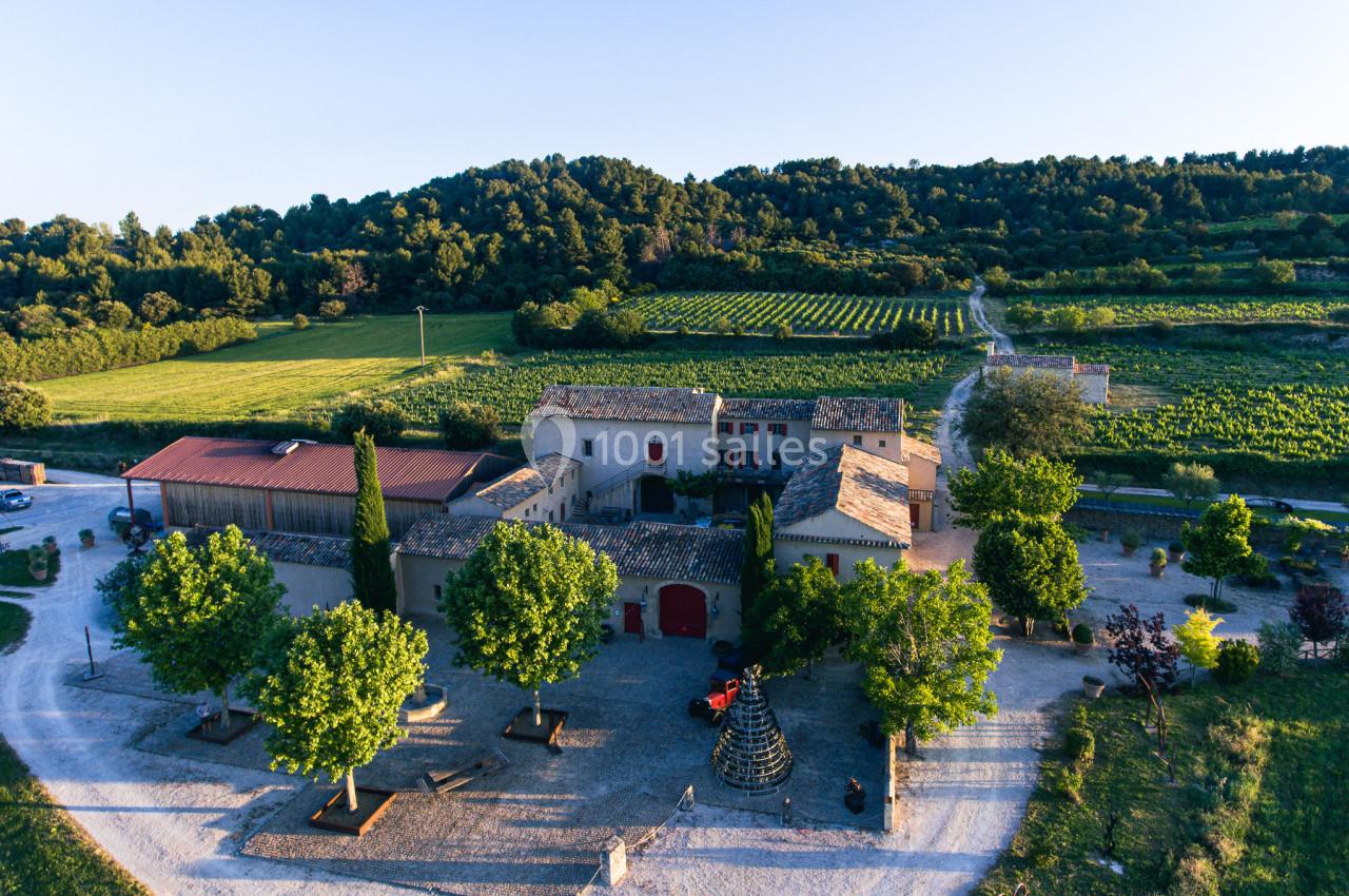 Vue aérienne d'un domaine viticole entouré de vignes et de collines verdoyantes sous un ciel dégagé.