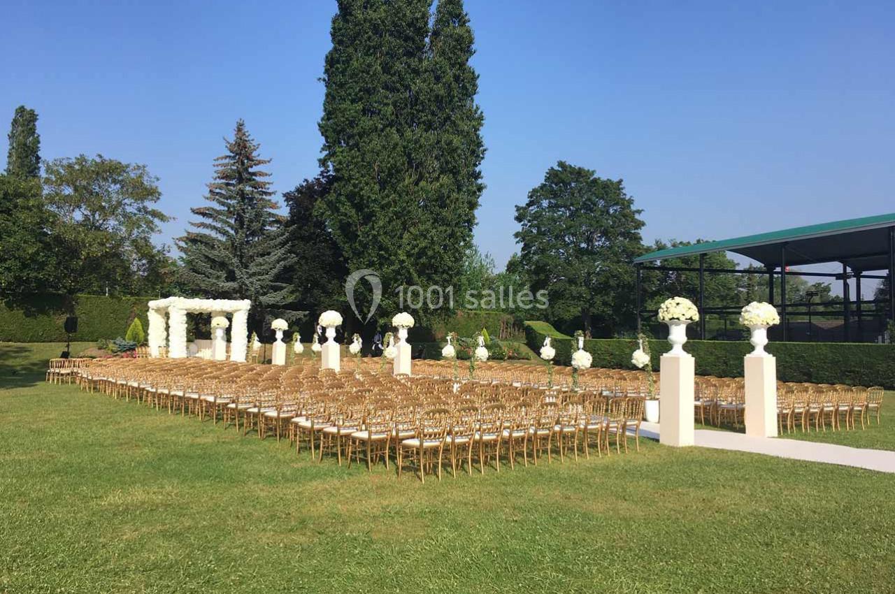 Chaises dorées alignées en extérieur devant une arche fleurie blanche, entourées de colonnes décorées de bouquets.