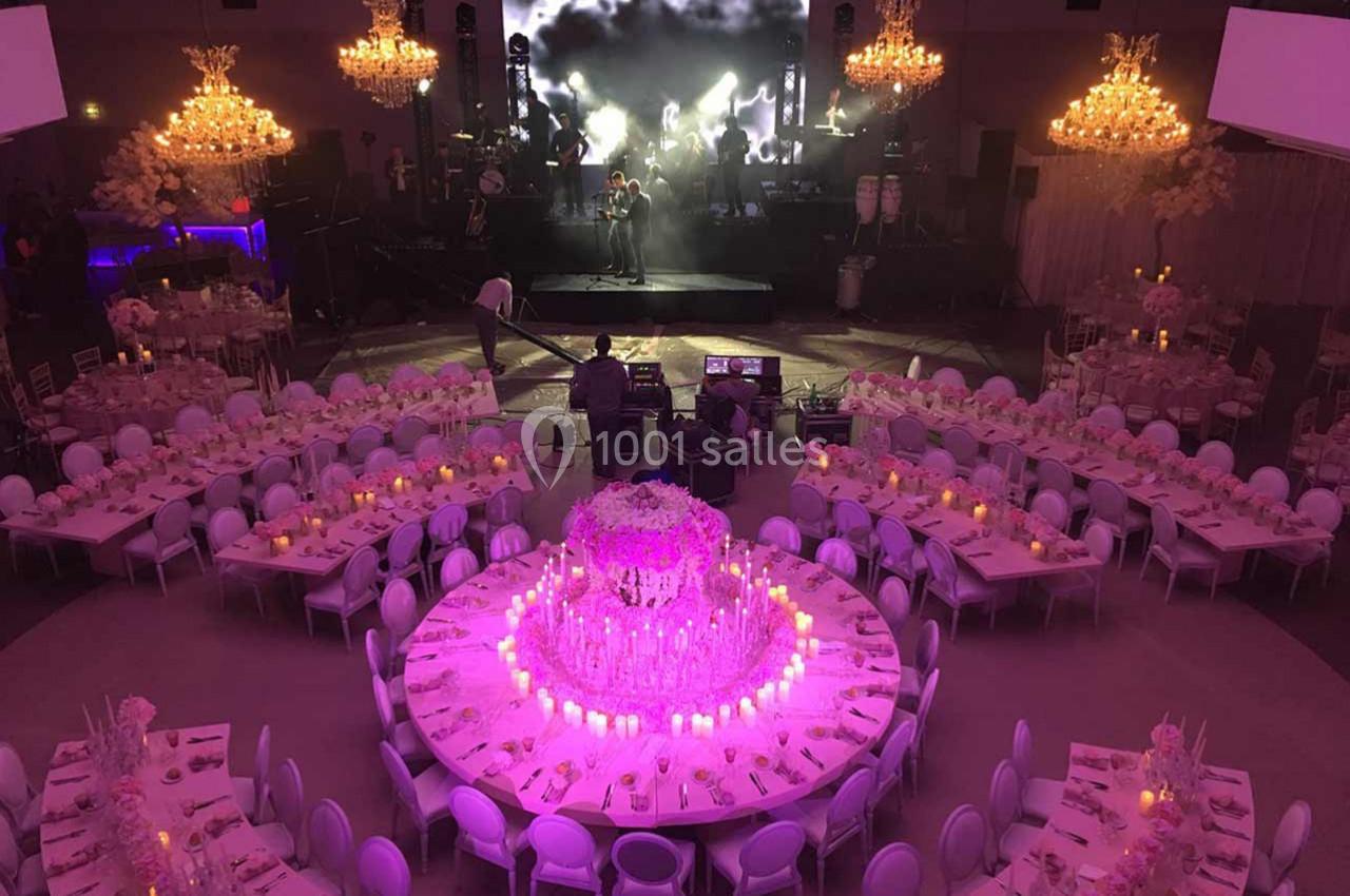 Salle de réception décorée avec des tables rondes, des chandeliers lumineux et une scène avec un écran en arrière-plan.