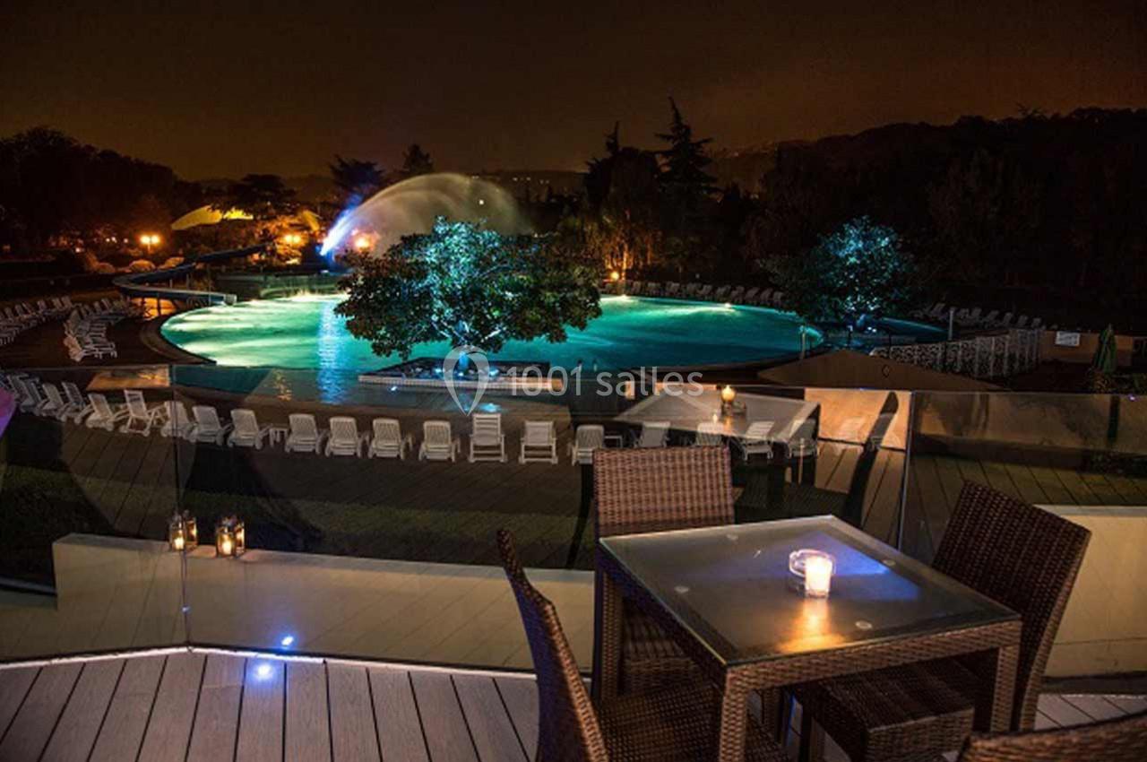 Piscine éclairée de nuit entourée de chaises longues, avec une terrasse en premier plan et des bougies allumées.