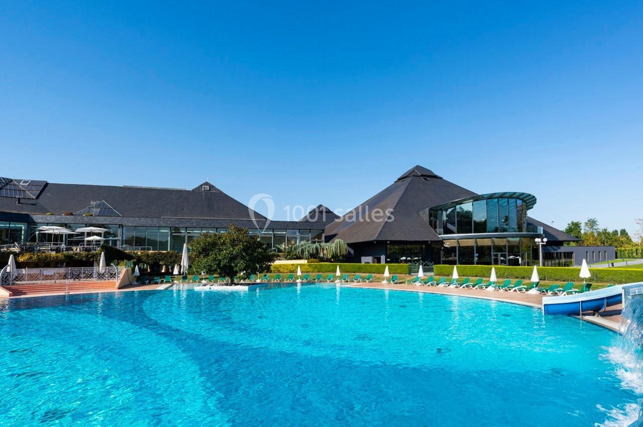 Piscine extérieure avec eau turquoise entourée de chaises longues, devant un bâtiment moderne sous un ciel bleu.