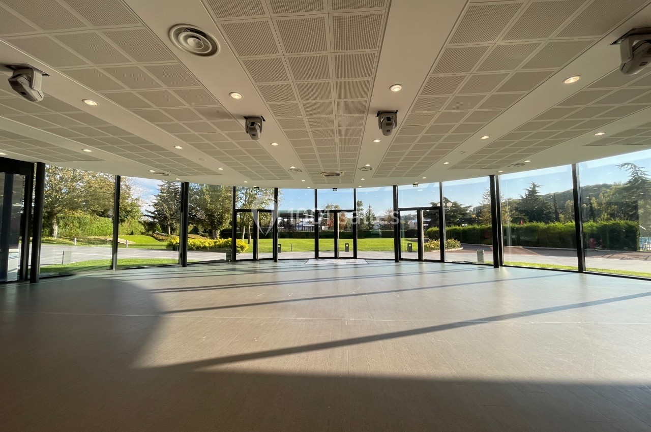 Salle lumineuse avec de grandes baies vitrées donnant sur un espace extérieur verdoyant et ensoleillé.