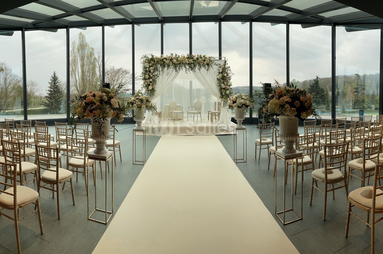 Allée centrale menant à une arche florale décorée pour une cérémonie de mariage, entourée de chaises dorées.