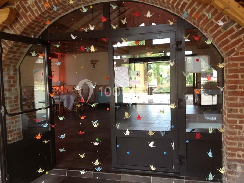 Guirlandes de grues en papier suspendues devant une porte vitrée dans un cadre intérieur lumineux.