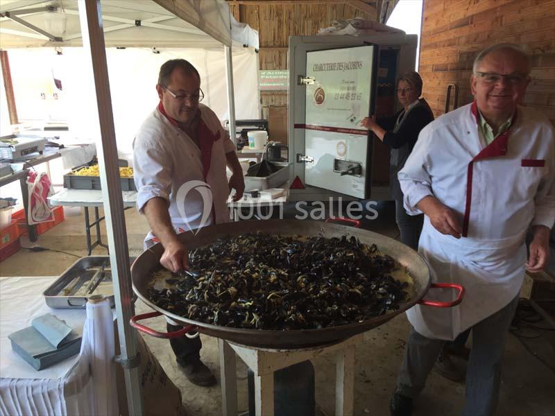 Deux hommes en tablier cuisinent une grande poêlée de moules dans un espace couvert lors d'un événement.