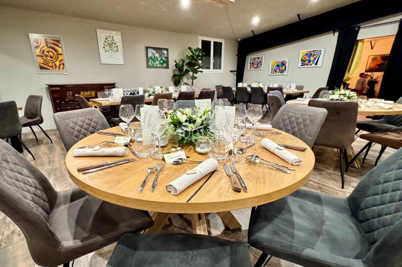 Salle de réception avec tables rondes dressées, décorations florales et chaises rembourrées dans un cadre moderne.