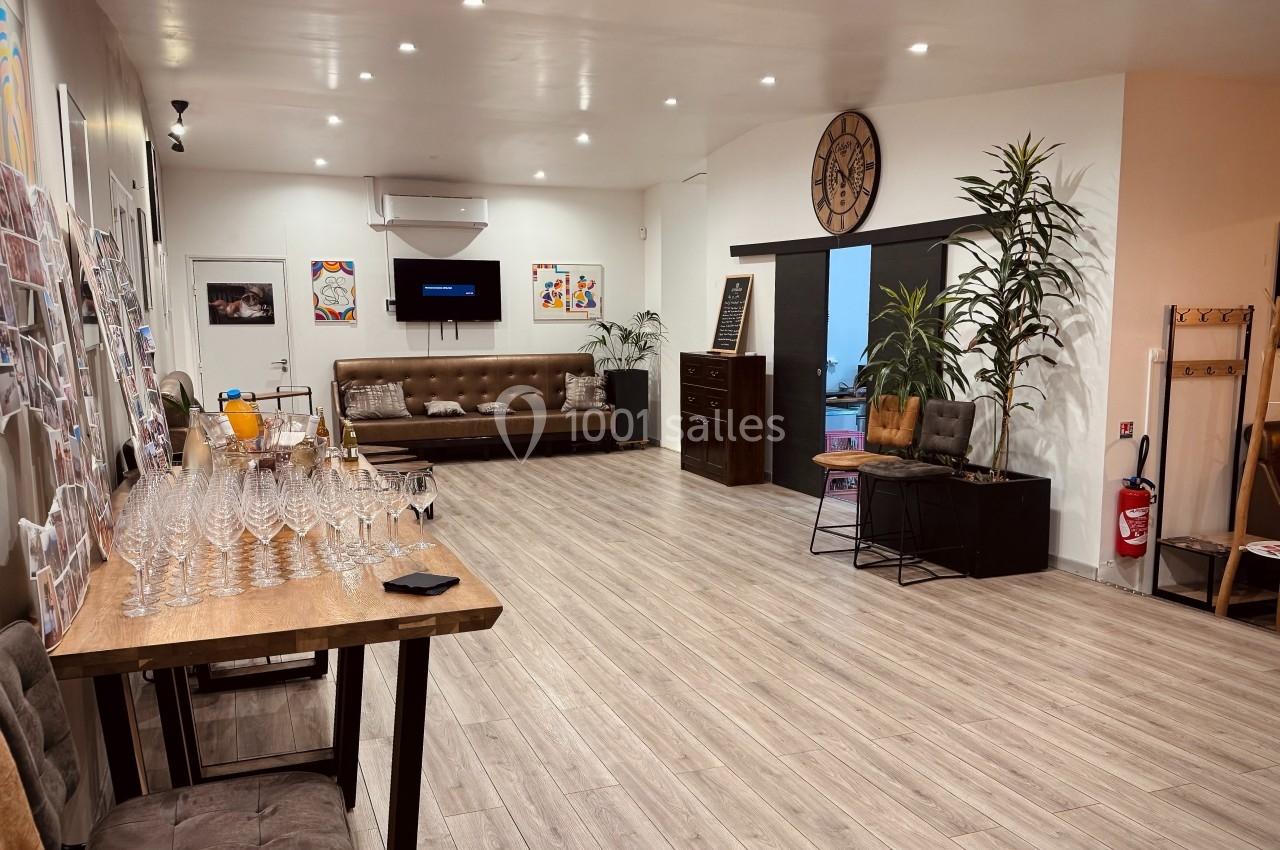 Salle lumineuse avec parquet, canapés, plantes, table avec verres alignés et décorations murales colorées.