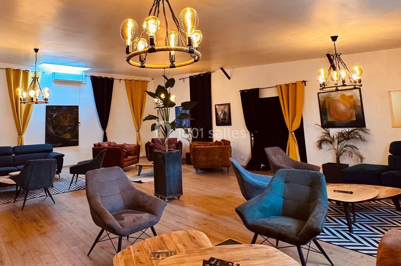 Salle lumineuse avec mobilier moderne, fauteuils confortables, tables basses en bois et éclairage chaleureux.