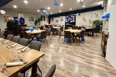 Coucher de soleil rougeoyant derrière une rangée d'arbres, vu depuis une terrasse avec mobilier et voitures garées.