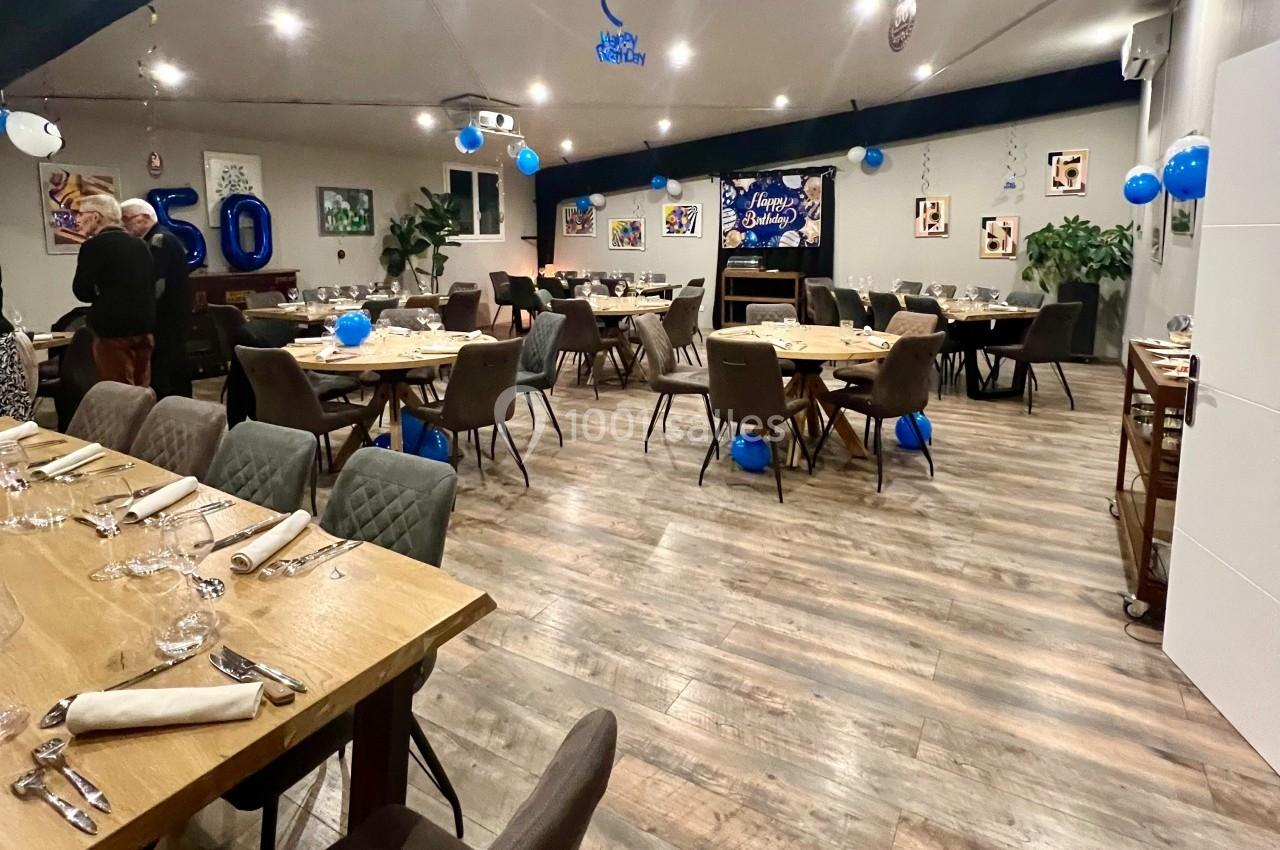 Salle décorée pour une fête avec ballons bleus et blancs, tables dressées et affiches aux murs.