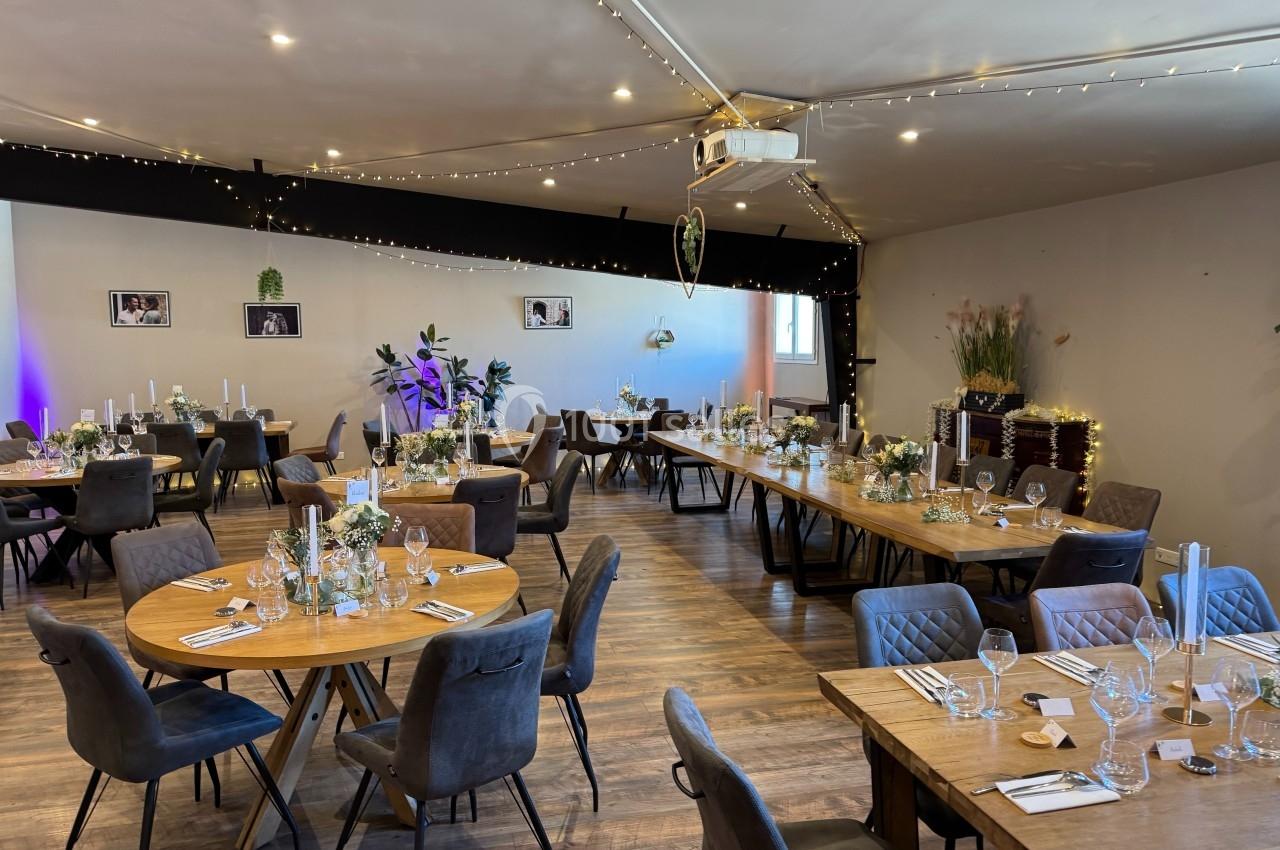Salle de réception décorée avec des tables rondes et rectangulaires, ornées de fleurs et de bougies, éclairage chaleureux.