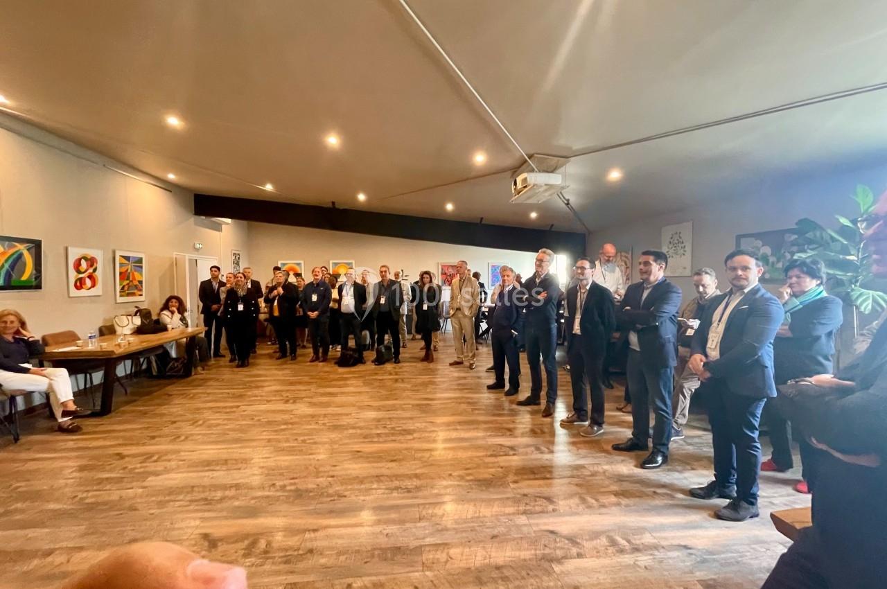 Groupe de personnes debout en cercle dans une grande salle lumineuse avec des œuvres d'art accrochées aux murs.