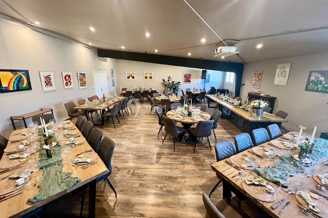 Salle de réception avec tables en bois dressées, décorations élégantes et œuvres d'art accrochées aux murs.