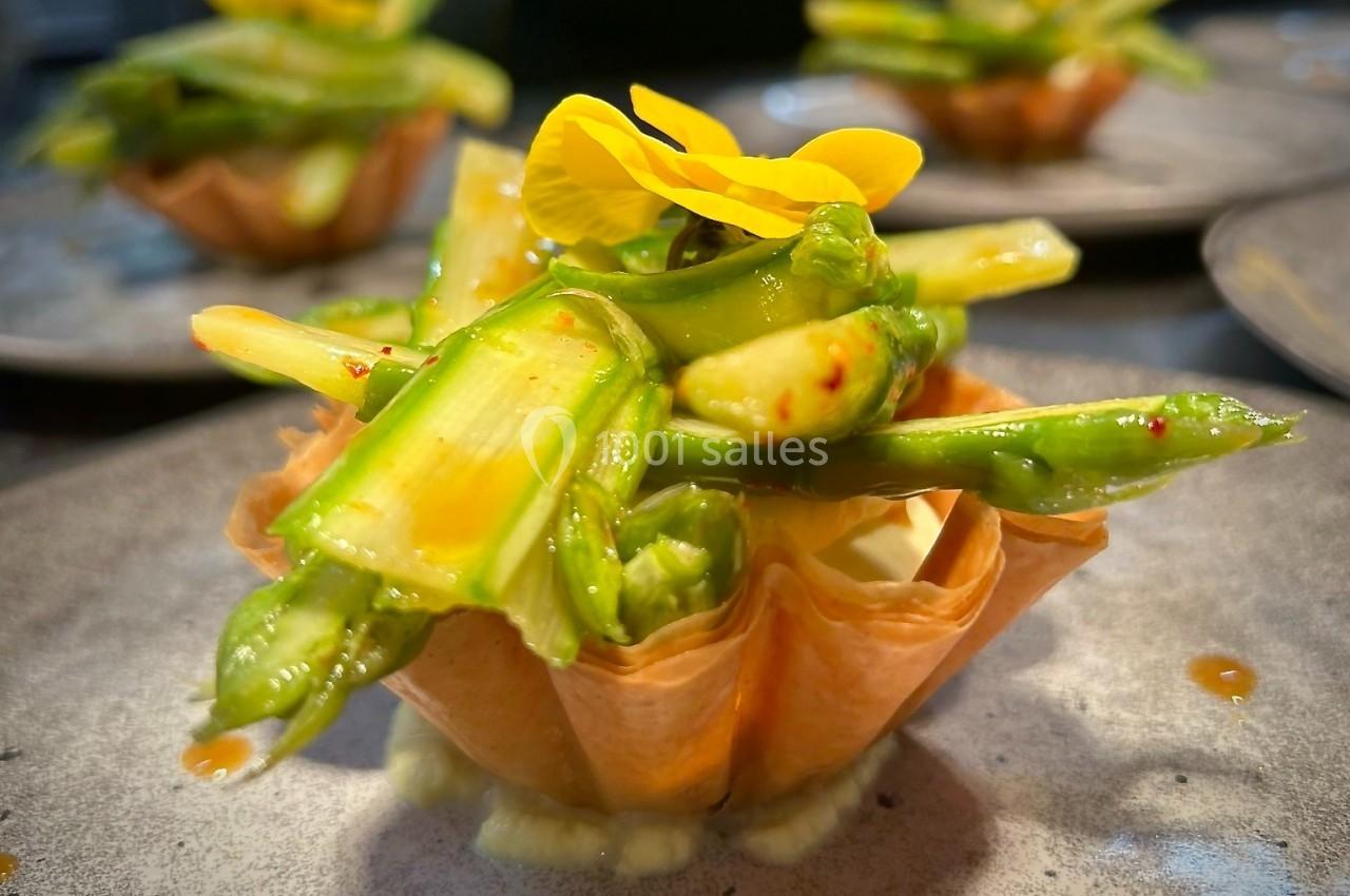 Tartelette garnie d'asperges vertes croquantes et décorée d'une fleur jaune, présentée sur une assiette grise.