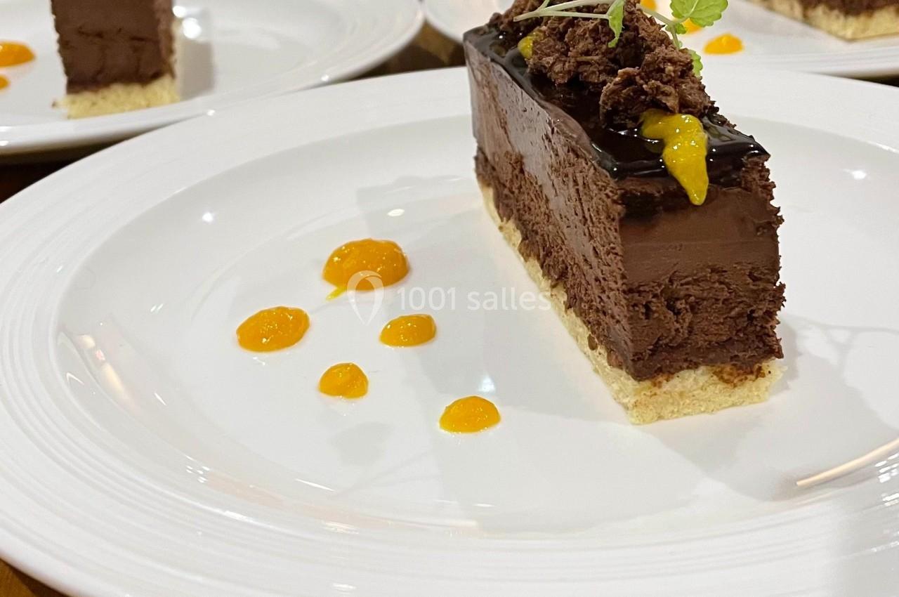 Part de gâteau au chocolat décorée de feuilles de menthe et de coulis orange, servie sur une assiette blanche.