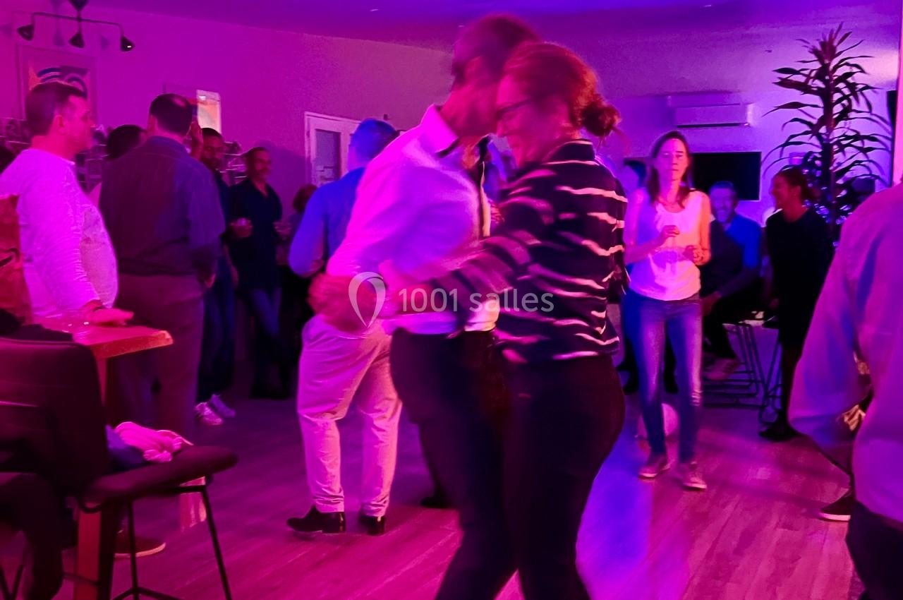 Deux personnes dansent dans une salle éclairée par des lumières colorées, entourées de spectateurs.