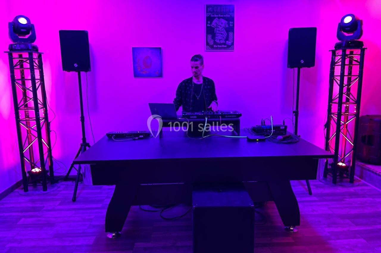 Un DJ mixe sur une table de mixage dans une salle éclairée par des lumières violettes et roses, entouré d'équipements audio.