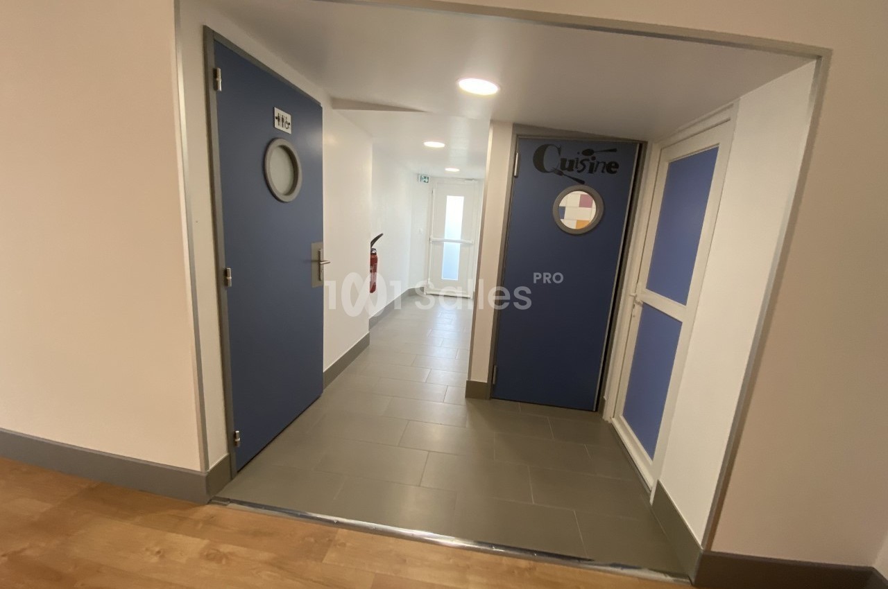 Couloir intérieur avec portes bleues, dont une indiquant ’Cuisine’, sol en carrelage gris et parquet au premier plan.