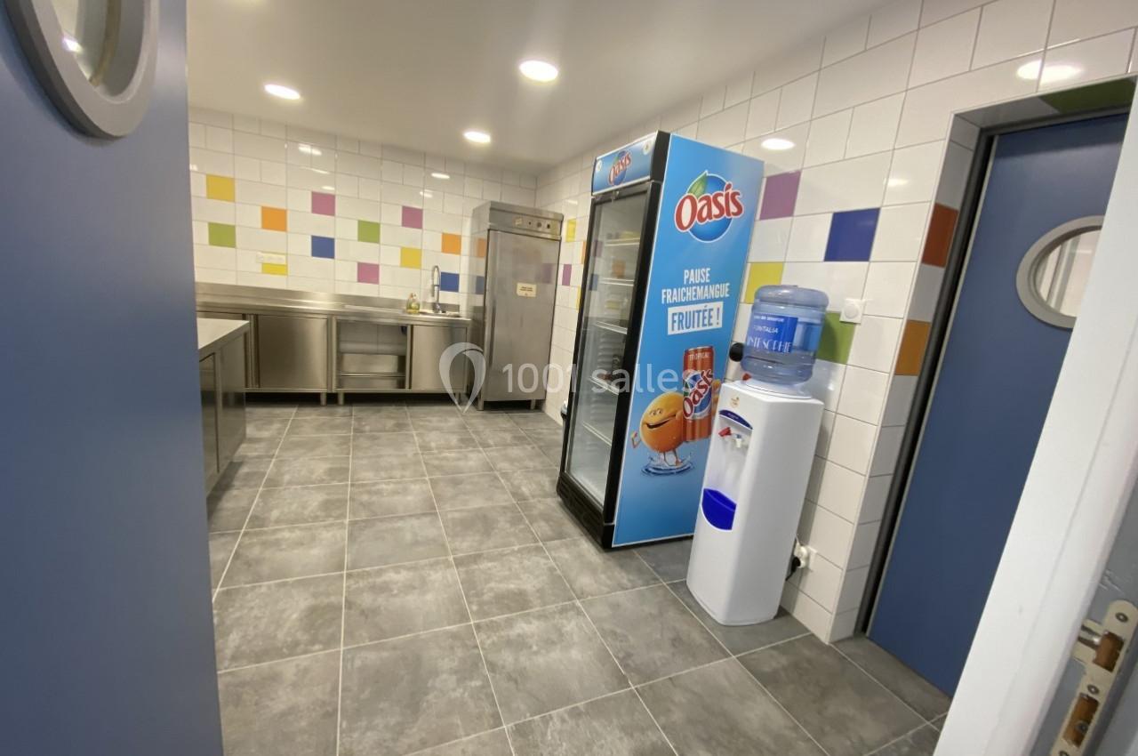 Cuisine professionnelle avec carrelage mural coloré, réfrigérateur, distributeur d'eau et équipements en inox.