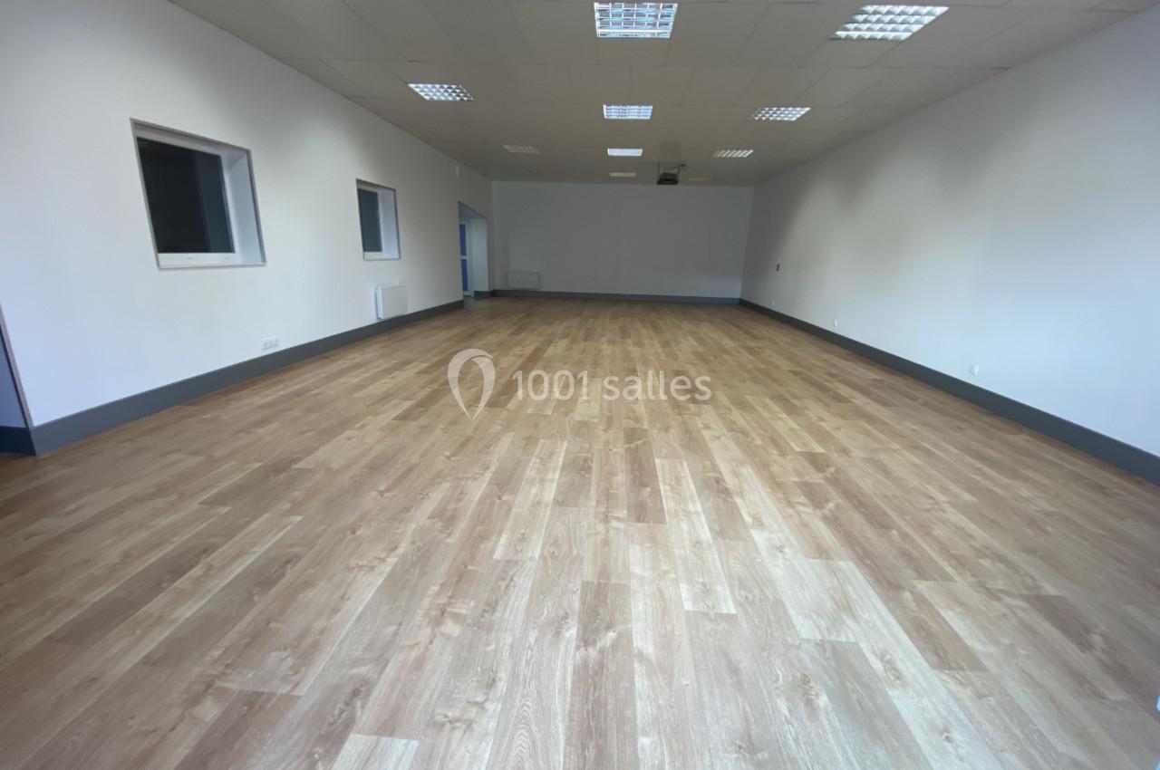 Salle vide avec un sol en parquet clair, murs blancs et plafond équipé de dalles lumineuses.