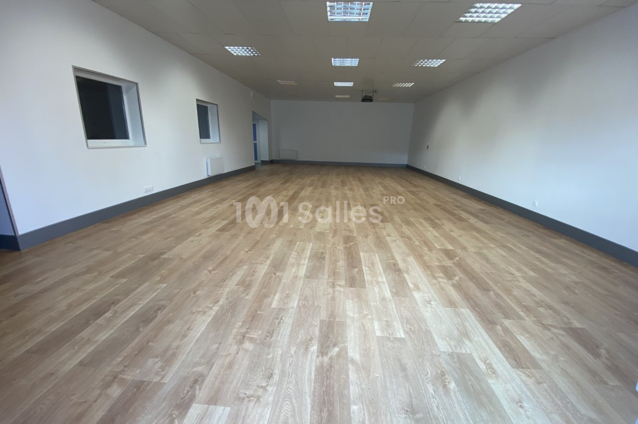 Salle vide avec un sol en parquet clair, murs blancs et plafond équipé de dalles lumineuses.
