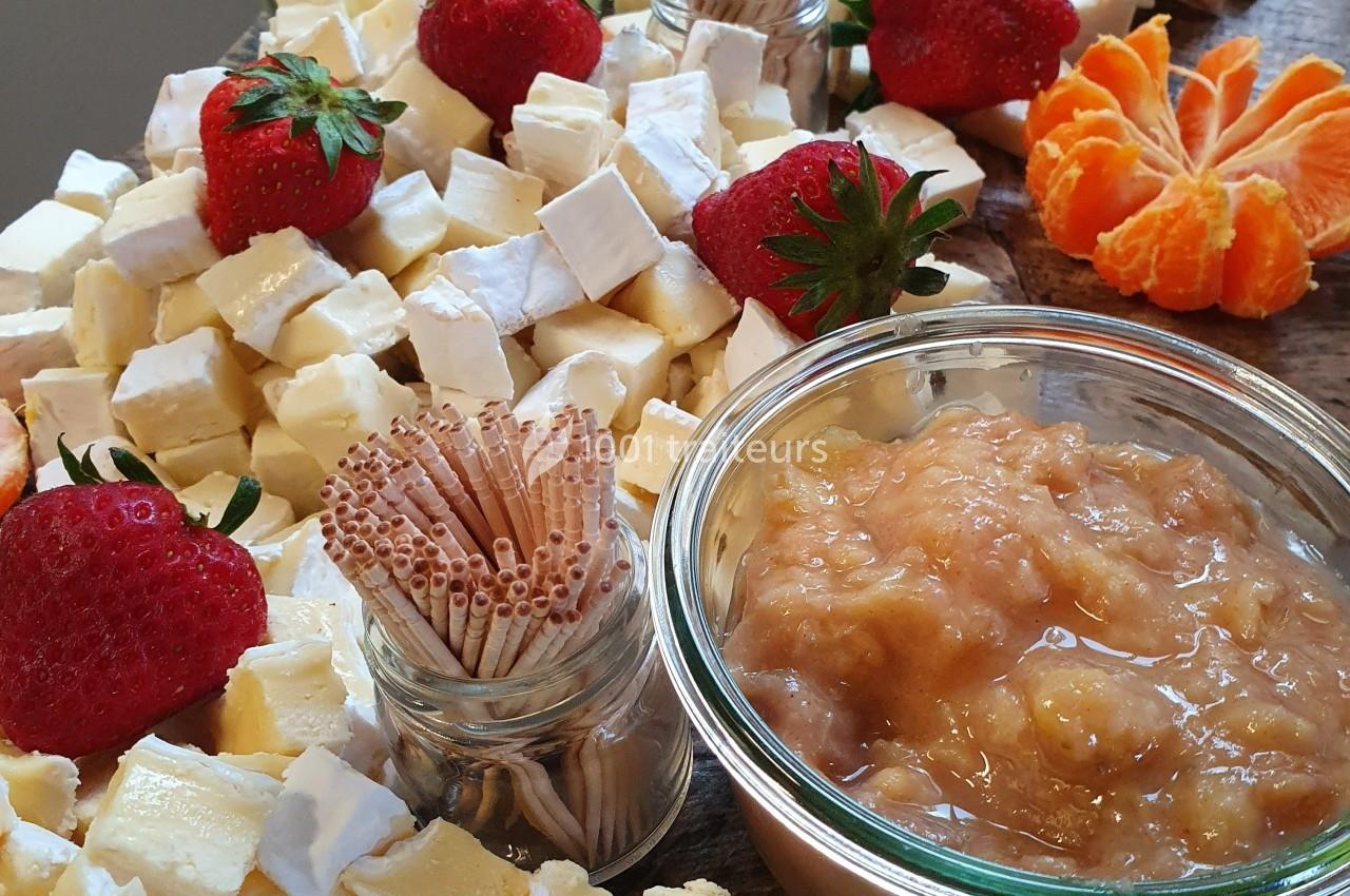 Plateau de fromages variés avec fraises, clémentine, confiture et bâtonnets en bois pour le service.