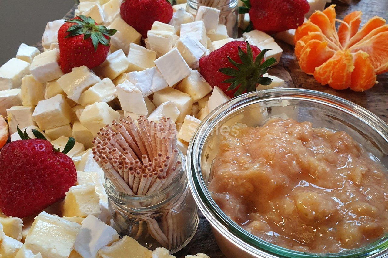 Plateau de fromages variés avec fraises, clémentine, confiture et bâtonnets en bois pour le service.
