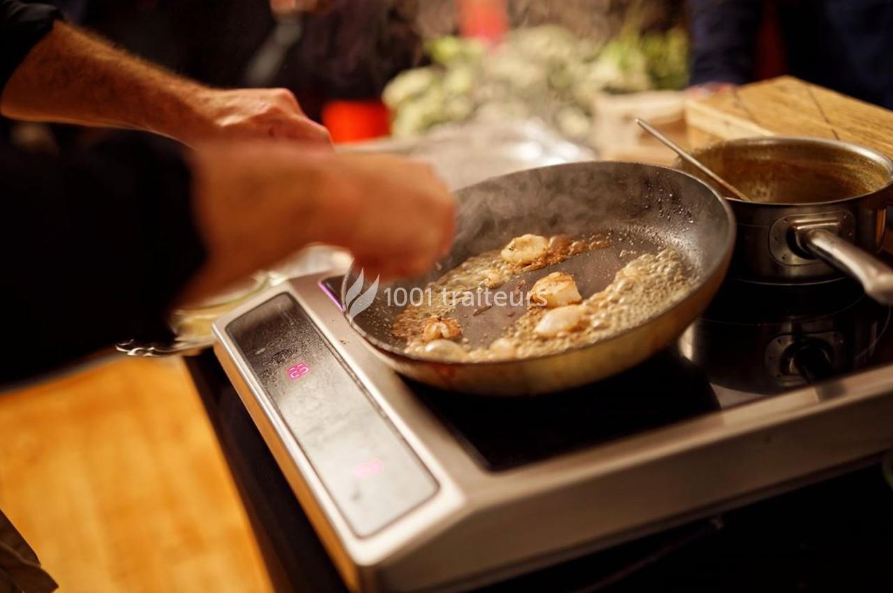 Une personne cuisine des noix de Saint-Jacques dans une poêle sur une plaque de cuisson.