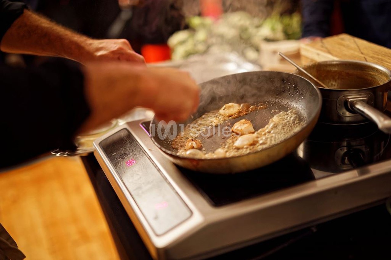 Une personne cuisine des noix de Saint-Jacques dans une poêle sur une plaque de cuisson.