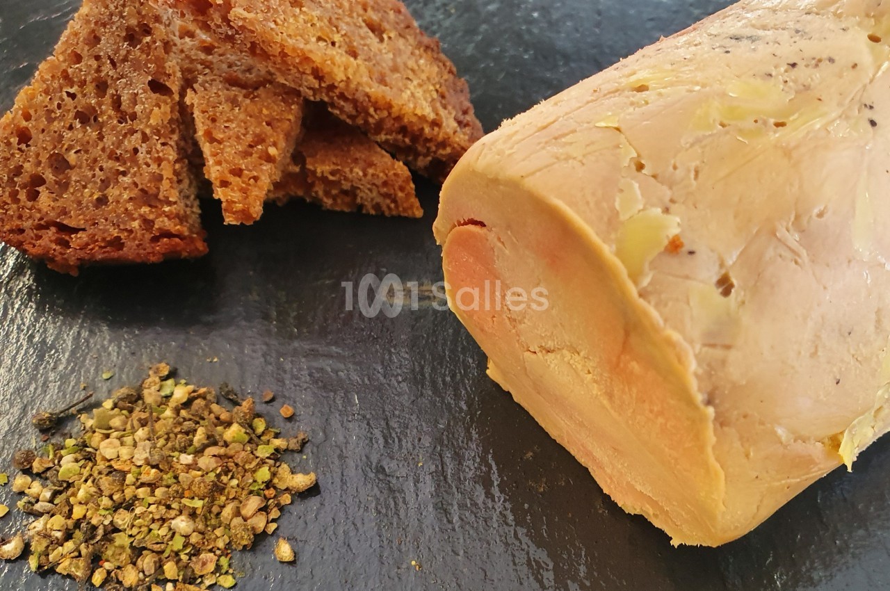 Bloc de foie gras accompagné de tranches de pain grillé et d'un mélange d'épices sur une ardoise noire.