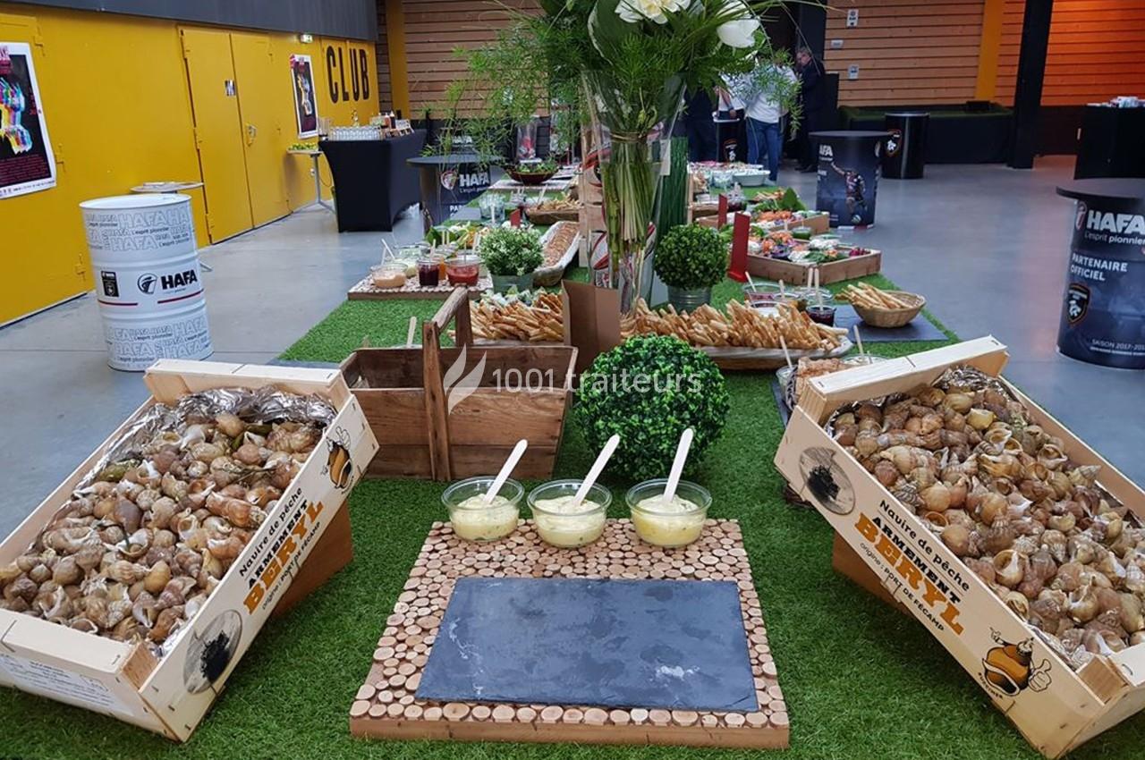 Buffet avec escargots en caisses, sauces en bols, décor végétal et table en bois dans une salle lumineuse.