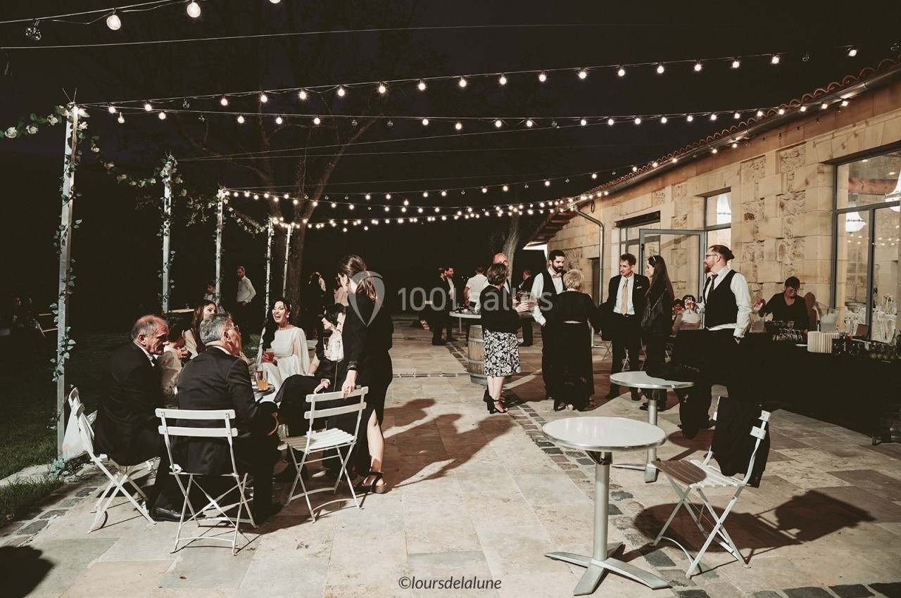 Personnes discutant et partageant un repas en soirée sur une terrasse éclairée par des guirlandes lumineuses.