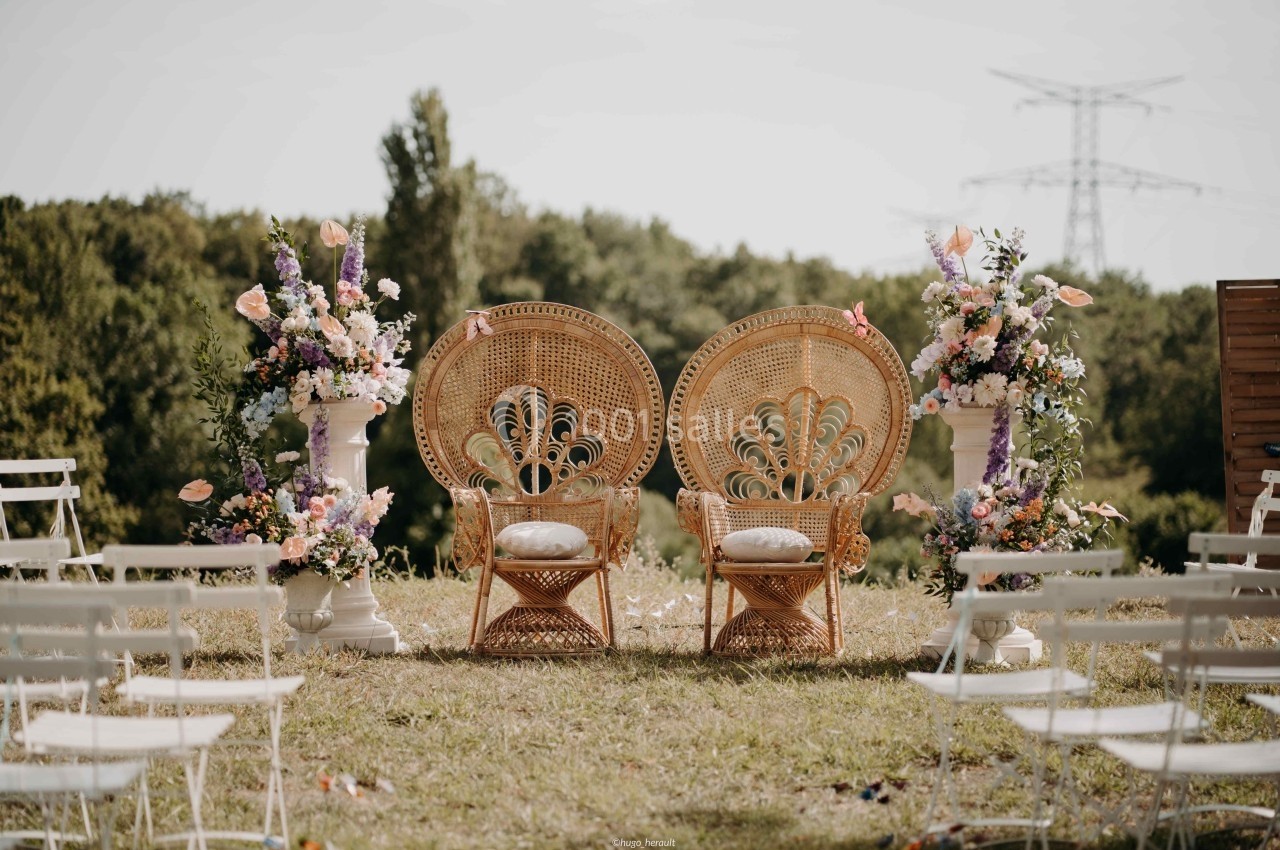 Deux fauteuils en rotin ornés de coussins, entourés de compositions florales, disposés en extérieur sur une pelouse.
