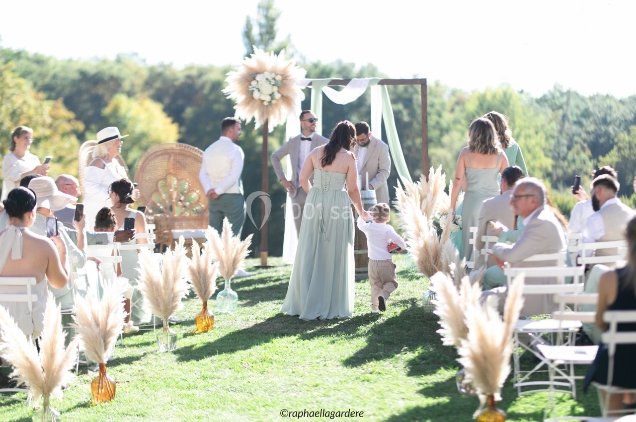 Cérémonie de mariage en extérieur avec invités assis, décor champêtre et mariés au centre de l'allée.
